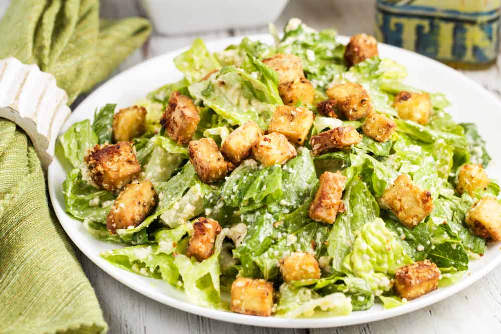 A white plate of Vegan Caesar Salad with Crunchy Sesame-Tofu Croutons stacked up