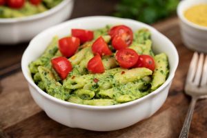 A white bowl filled with avocado penne pasta topped with cherry tomatoes.