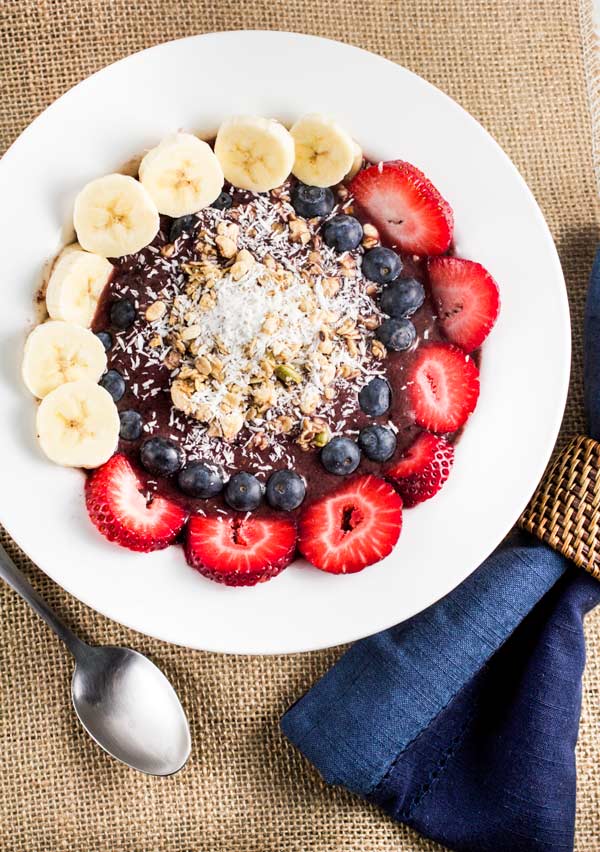 An overhead image of an acai bowl filled with bananas, strawberries, blueberries and coconut.