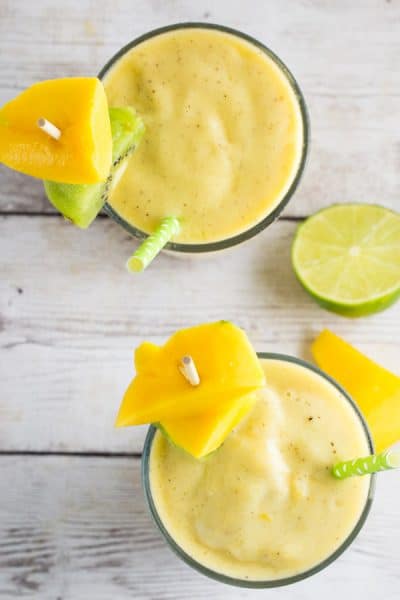 An overhead shot of 2 glasses of mango kiwi smoothies on a gray background.