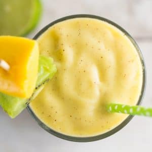 An overhead shot of a glass of Mango Kiwi Smoothie with a green straw