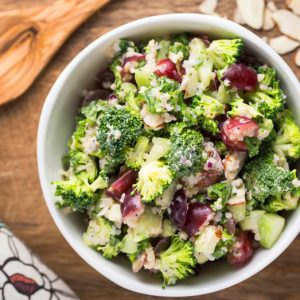 A bowl of broccoli quinoa salad on a wooden background with a large wooden spoon and sliced almonds
