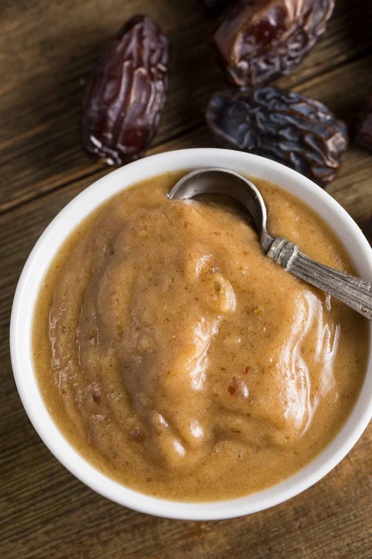 A white bowl filled with date paste with whole dates in the background.