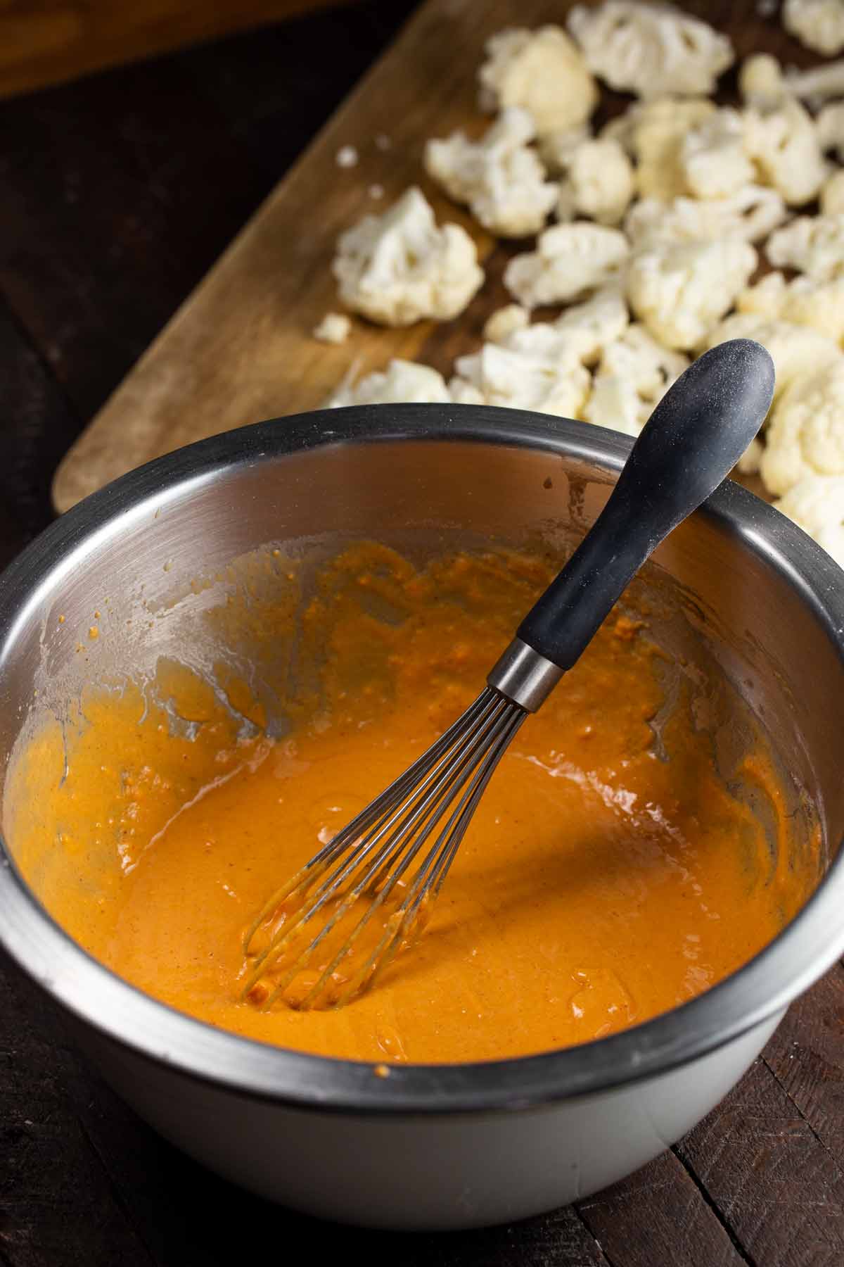 Bowl of buffalo cauliflower sauce with a whisk.