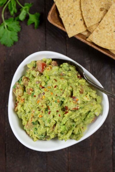 A bowl of guacamole with tacos on the side