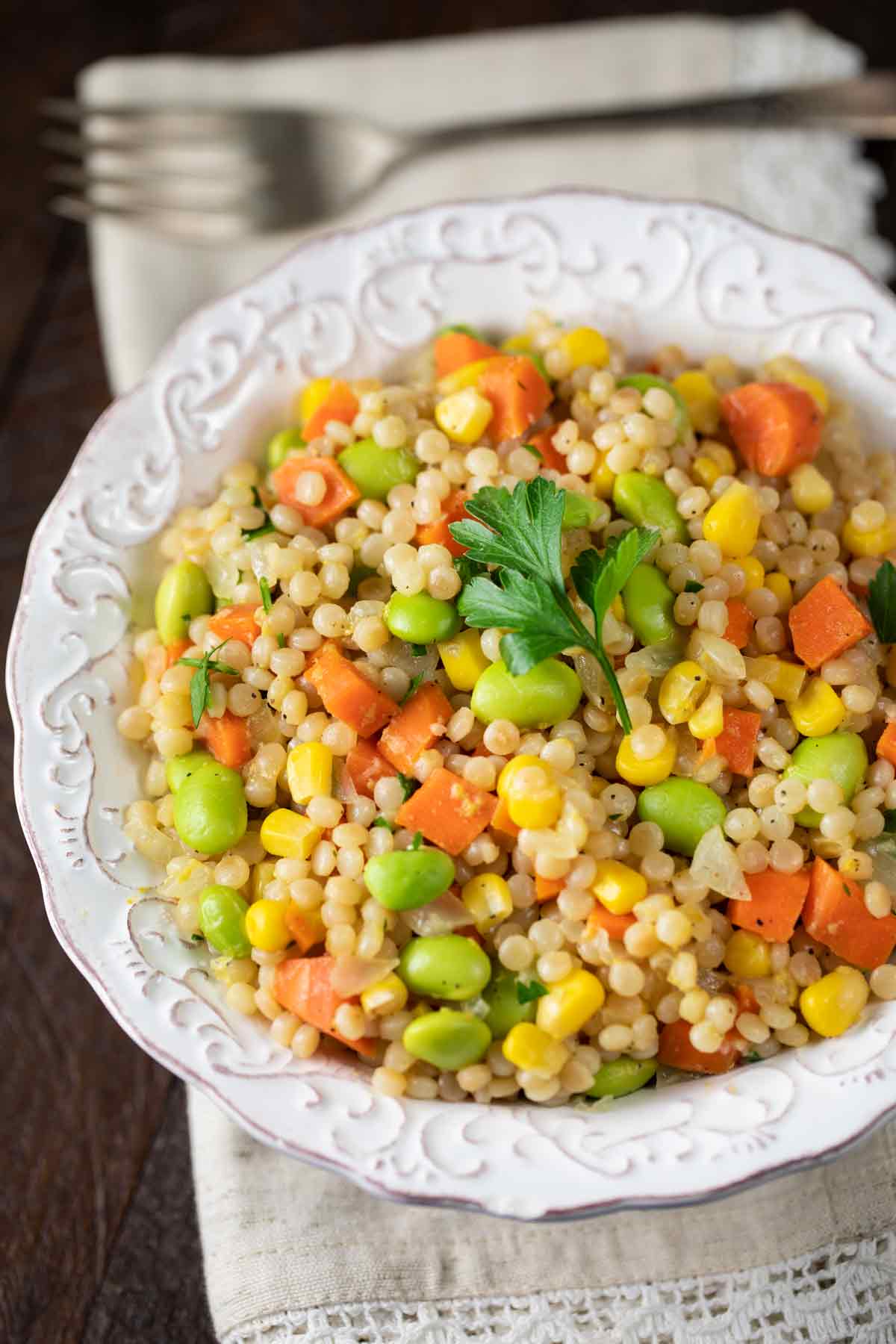 White decorative bowl filled with Israeli couscous with veggies.