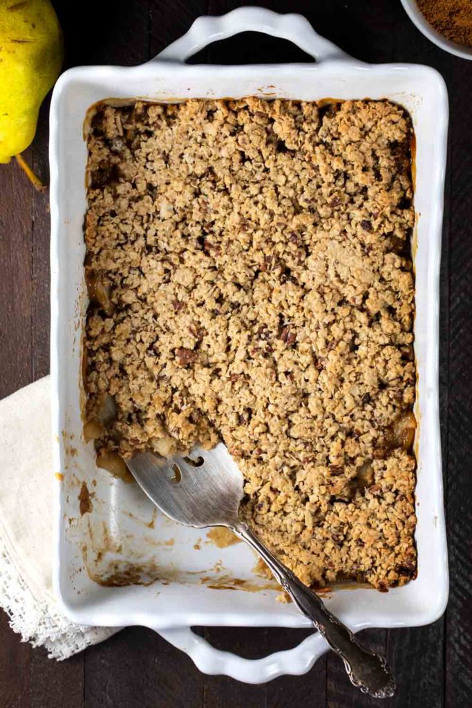 Pear crisp, in a white baking dish with one piece removed. 
