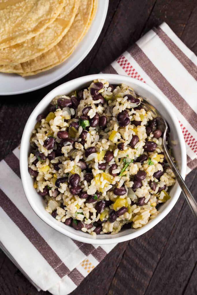 Black beans and rice in a white bowl with a fork and side of corn tortillas