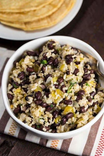 Black beans and rice in a white bowl with tortillas on the side.