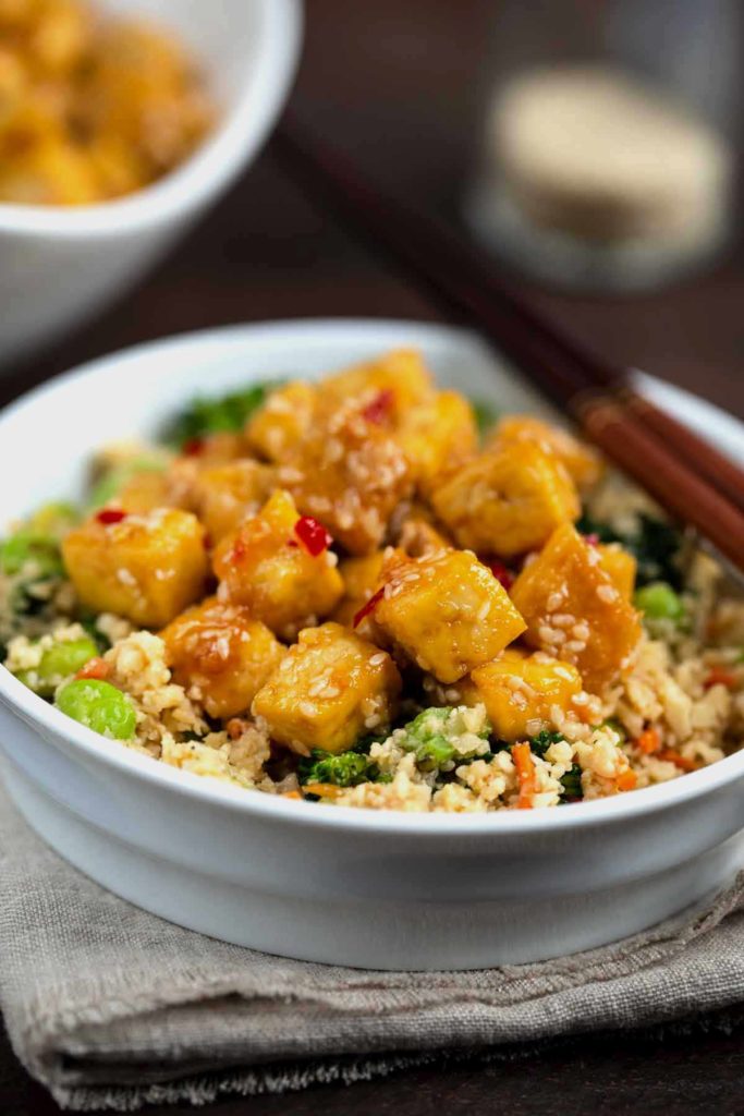 A white bowl filled with Cauliflower Rice Stir Fry topped with Crispy Sesame Tofu.