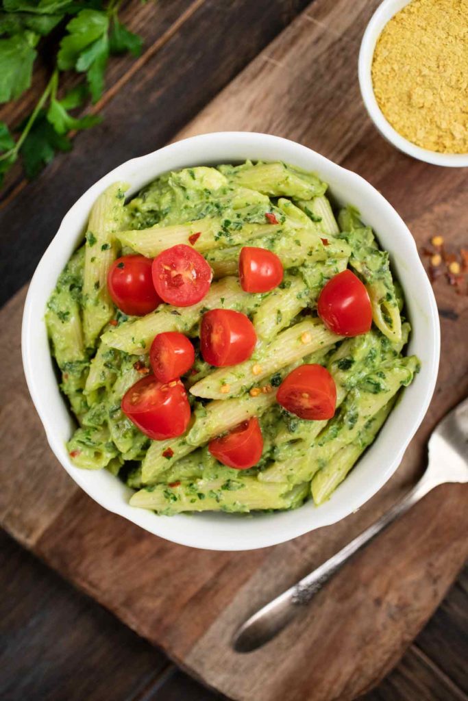 An overhead shot of a bowl of avocado pasta covered with cherry tomatoes. 