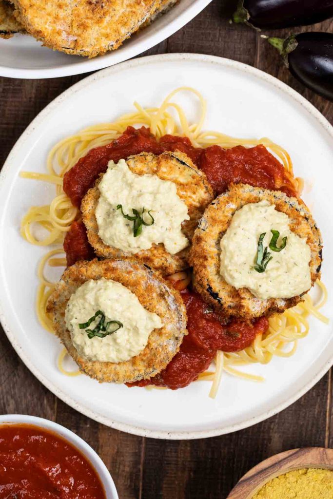 An overhead shot of a white plate filled with noodles, marinara and air fryer eggplant, topped with ricotta cheese. 