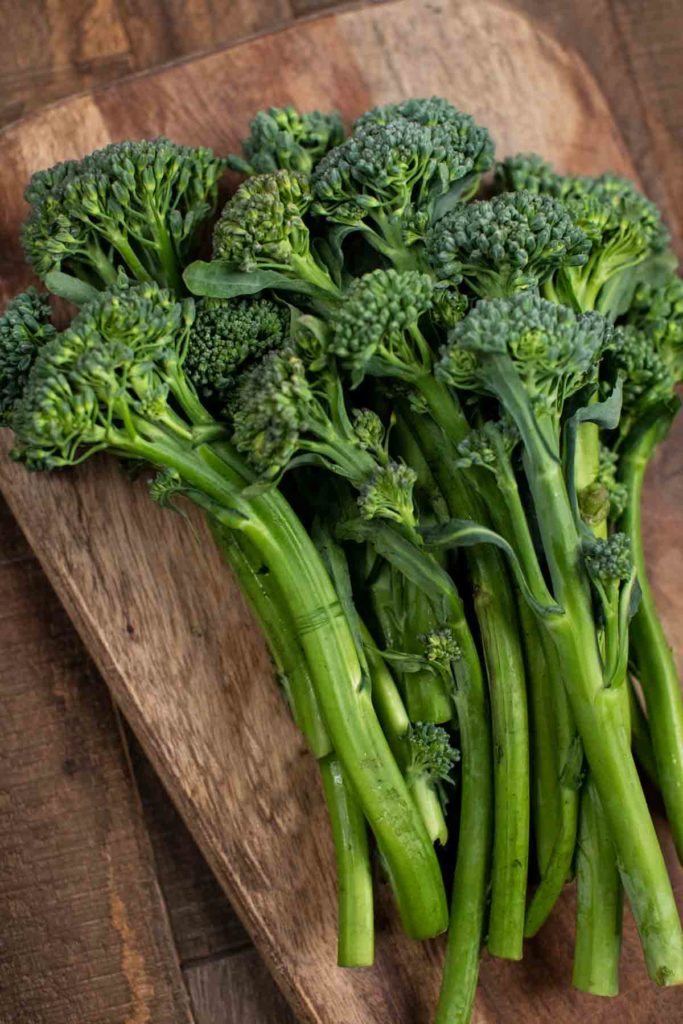 A cutting board covered with pieces of broccolini with stems. 