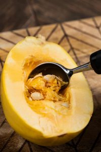 A raw spaghetti squash, with the seeds being removed by an ice cream scooper.