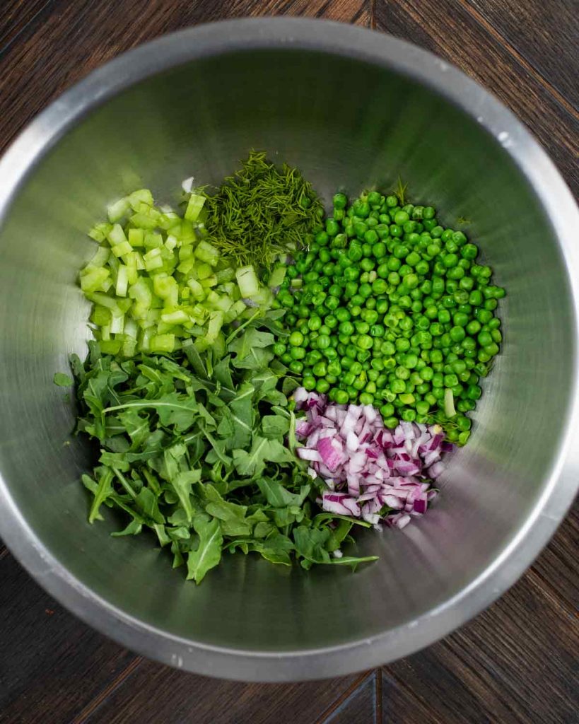 A large bowl filled with sweet peas, red onion, celery and arugula.