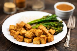 A white plate filled with air fryer tofu with broccolini and white rice in the background of the plate.