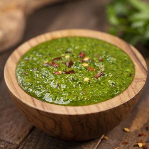 Chimichurri Sauce in a wooden bowl with crushed red pepper flakes on top.