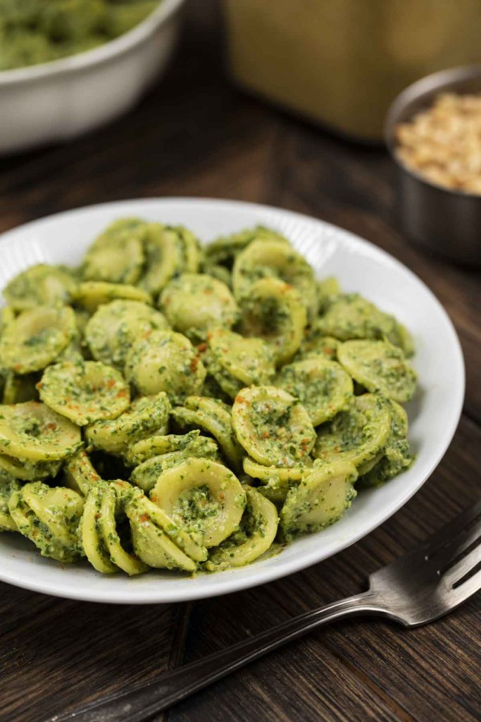 A side angle of a white plate filled with pasta noodles mixed in with a pesto sauce.