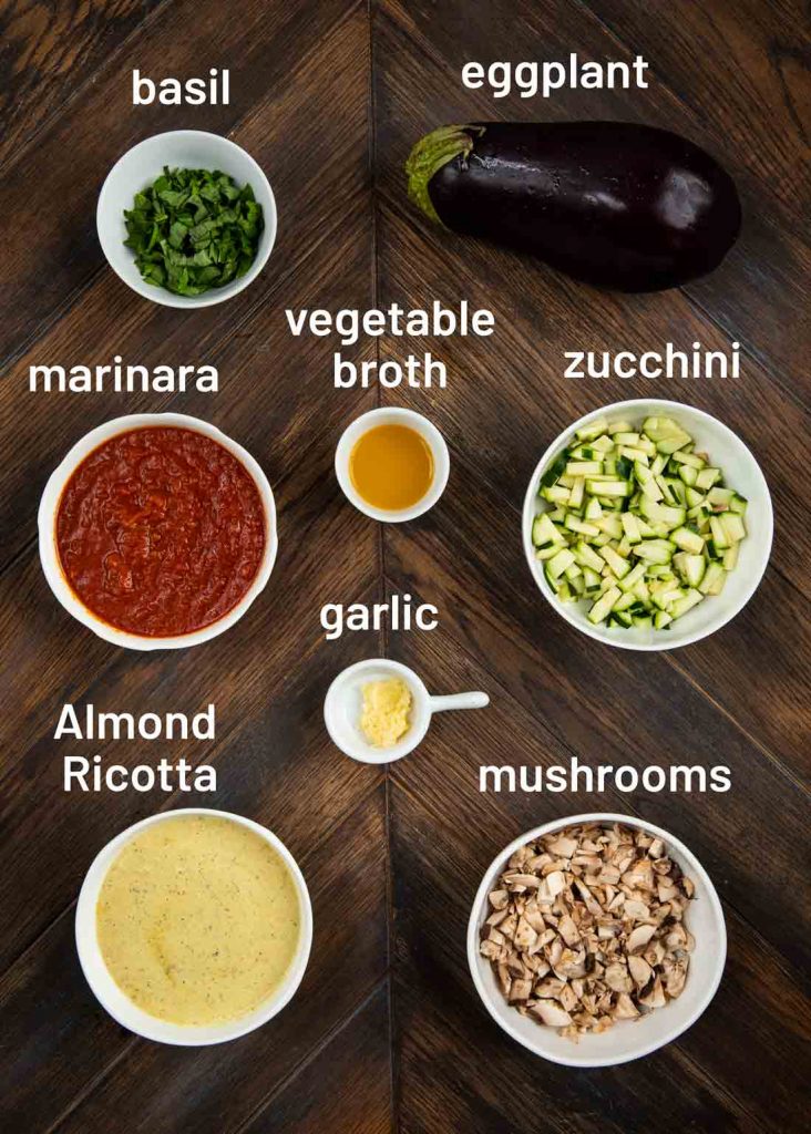 An overhead shot of the ingredients to make Eggplant Roll-Ups, including basil, eggplant, veggie broth, marinara, zucchini, mushrooms, garlic and Almond Ricotta.