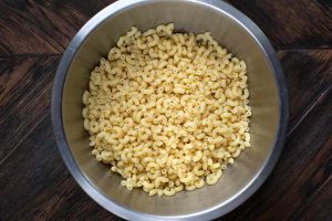 A stainless steel bowl of uncooked elbow macaroni