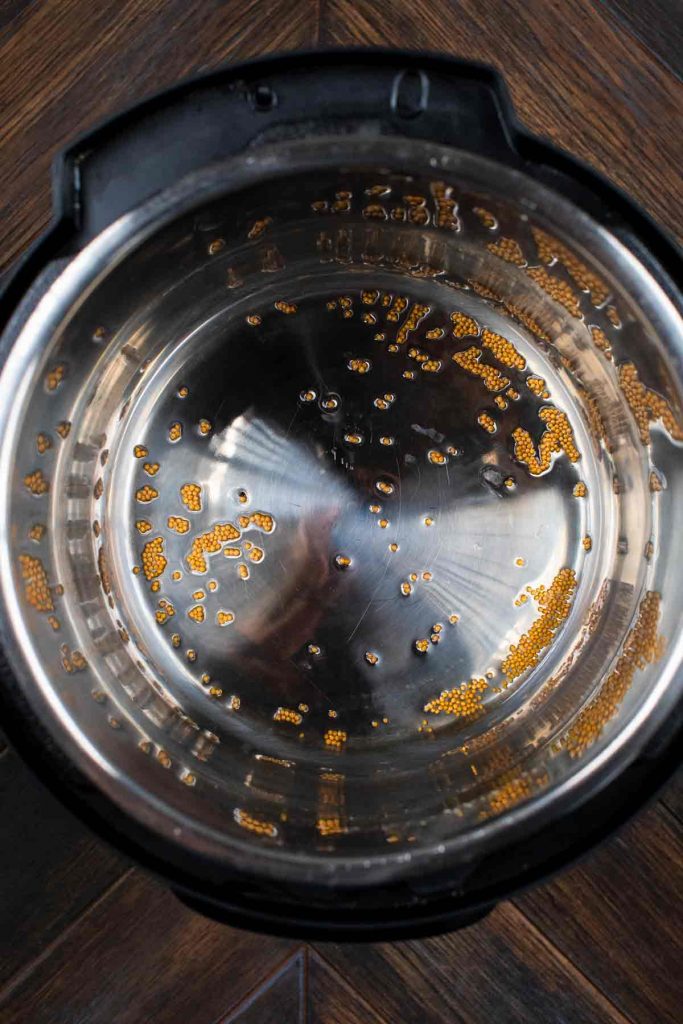 An overhead shot of an instant pot with mustard seeds and oil inside sautéing.