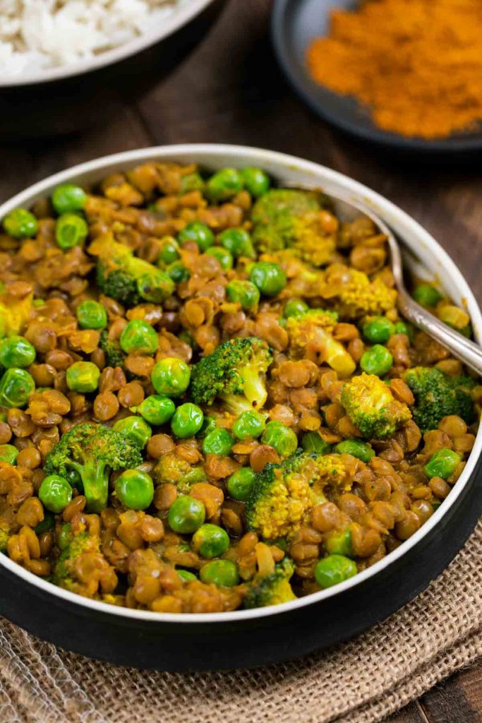 A bowl of curried lentils with broccoli and peas.