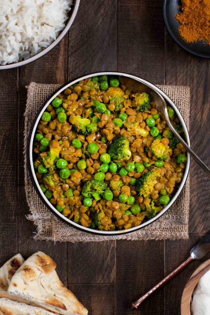 An overhead shot of a bowl of lentil curry with peas and broccoli.