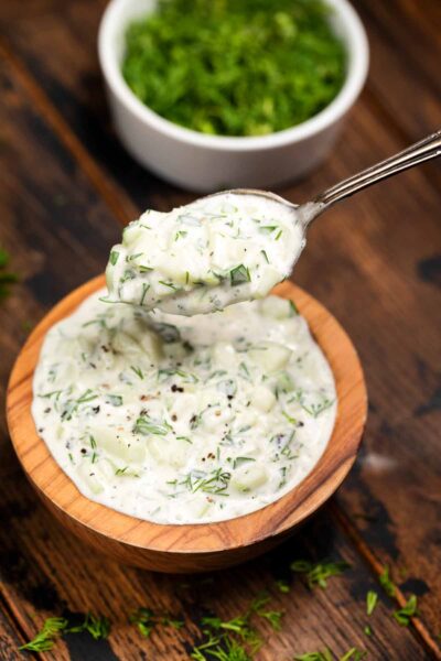 A wooden bowl filled with a cucumber tzaziki sauce, with a spoon.