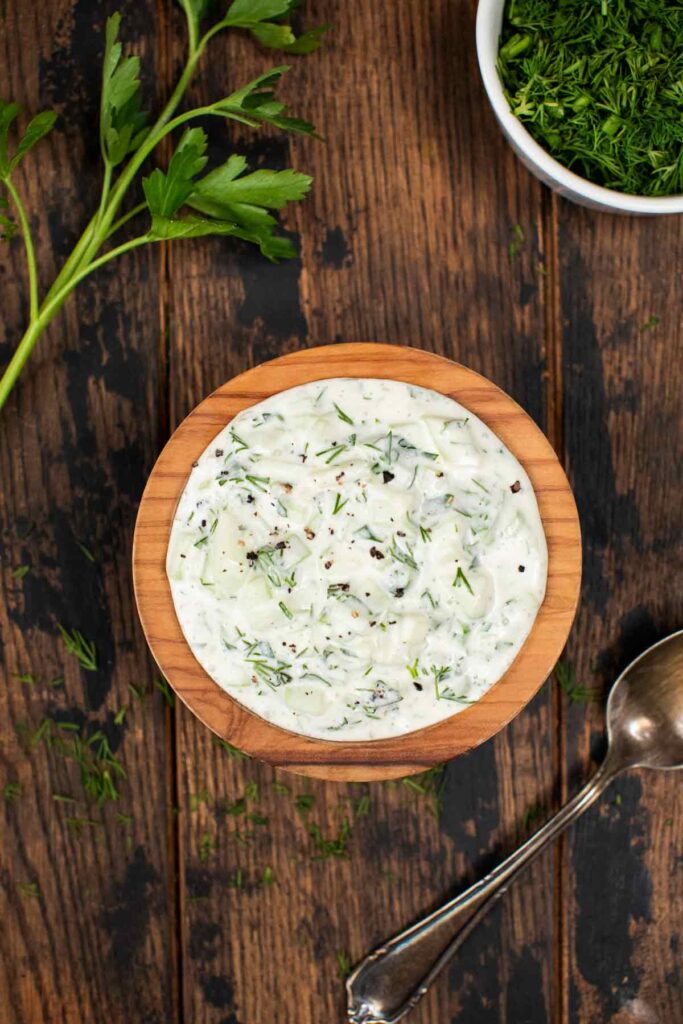 An overhead shot of a small bowl of vegan tzatziki sauce, with fresh parsley on the side.